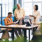 Outsourced Employee Benefits in Australia Concentrated multiracial colleagues in casual outfits reading documents and analyzing charts while gathering at table with laptops in contemporary office