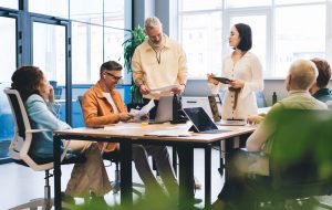 Concentrated multiracial colleagues in casual outfits reading documents and analyzing charts while gathering at table with laptops in contemporary office