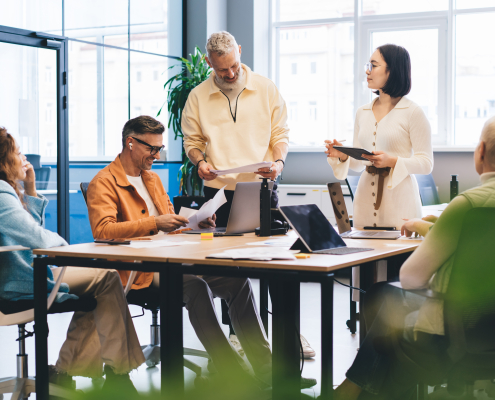 Concentrated multiracial colleagues in casual outfits reading documents and analyzing charts while gathering at table with laptops in contemporary office
