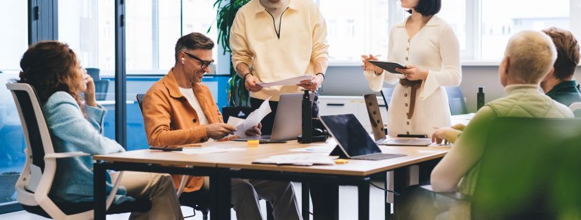 Concentrated multiracial colleagues in casual outfits reading documents and analyzing charts while gathering at table with laptops in contemporary office